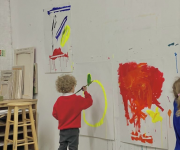A child making a large painting, pinned to a wall.