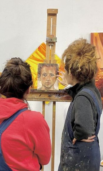 Two women discussing a small portrait painting on an easel.
