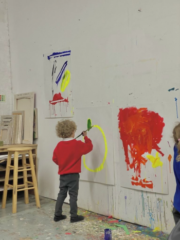 A child making a large painting, pinned to a wall.